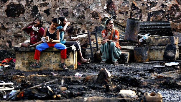 A family sits amid the burnt debris of their hut after a fire br